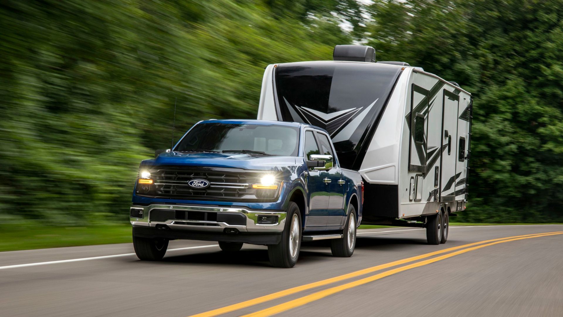 Dynamic front 3/4 shot of a blue 2024 Ford F-150 XLT towing a trailer.