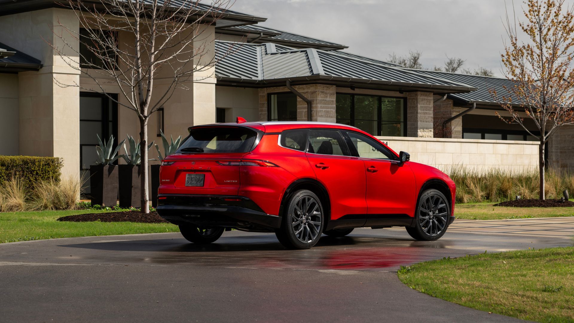Static rear 3/4 shot of a red 2025 Toyota Crown Signia Limited parked on a driveway outside of a house.