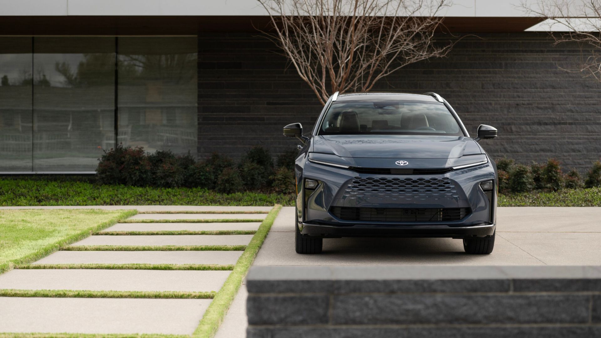 Static front-end shot of a gray 2025 Toyota Crown Signia Limited parked outside of a modern building.