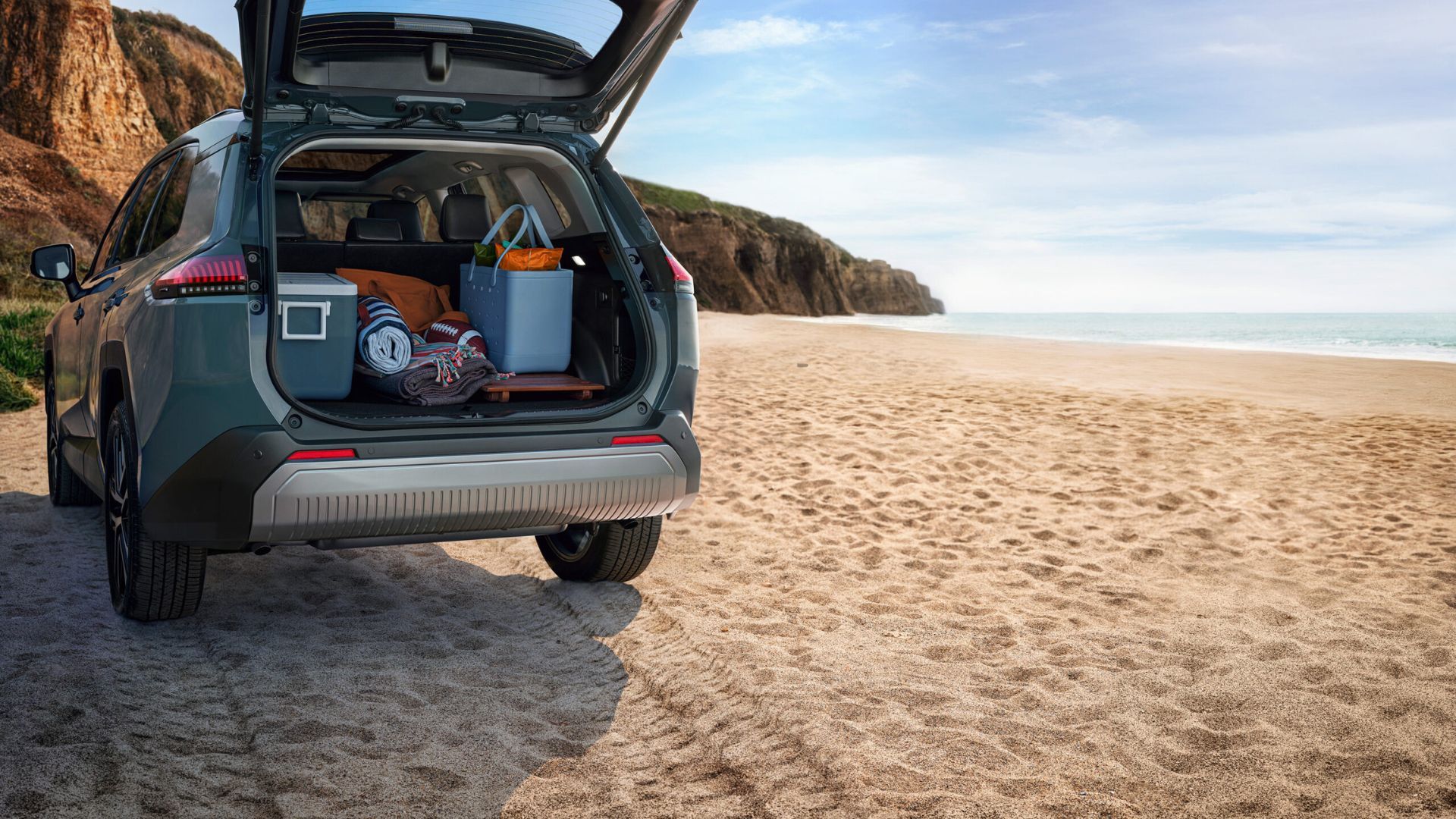 Static shot of a blue 2026 Toyota RAV4 Limited parked on a beach with it's trunk open filled with items.