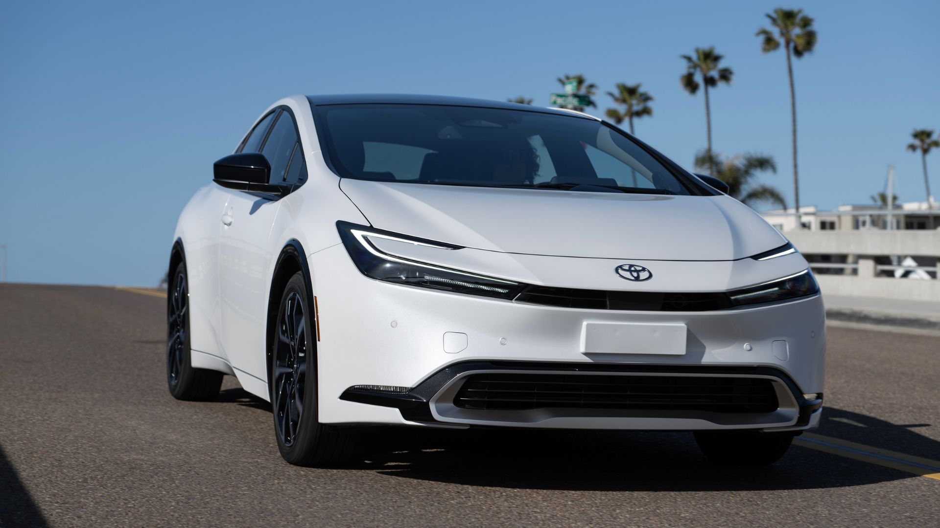 Dynaic front 3/4 shot of a white 2025 Toyota Prius PHEV XSE driving over a bridge.