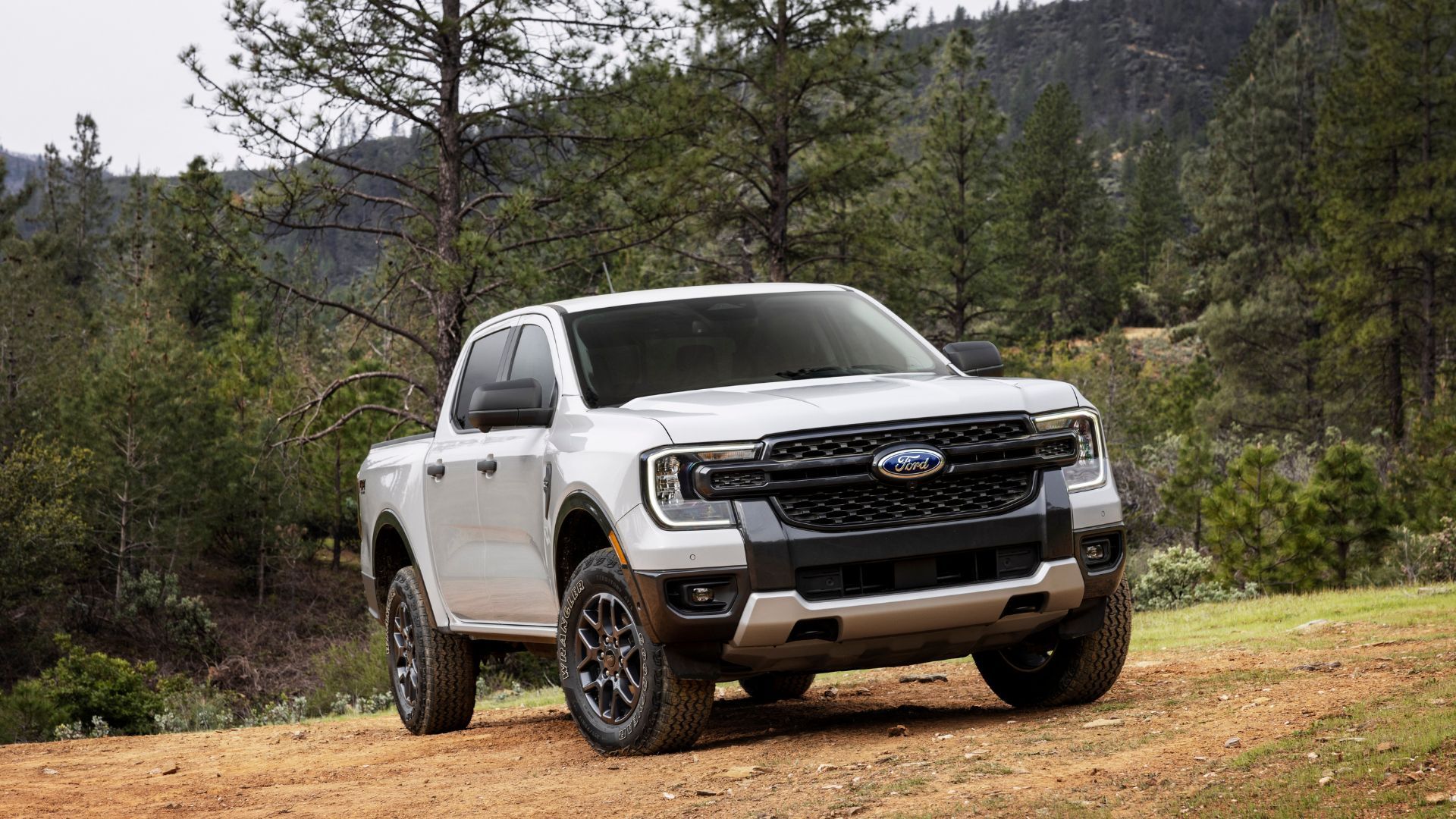 Front 3/4 shot of a white 2024 Ford Ranger parked on grass with trees in the background.