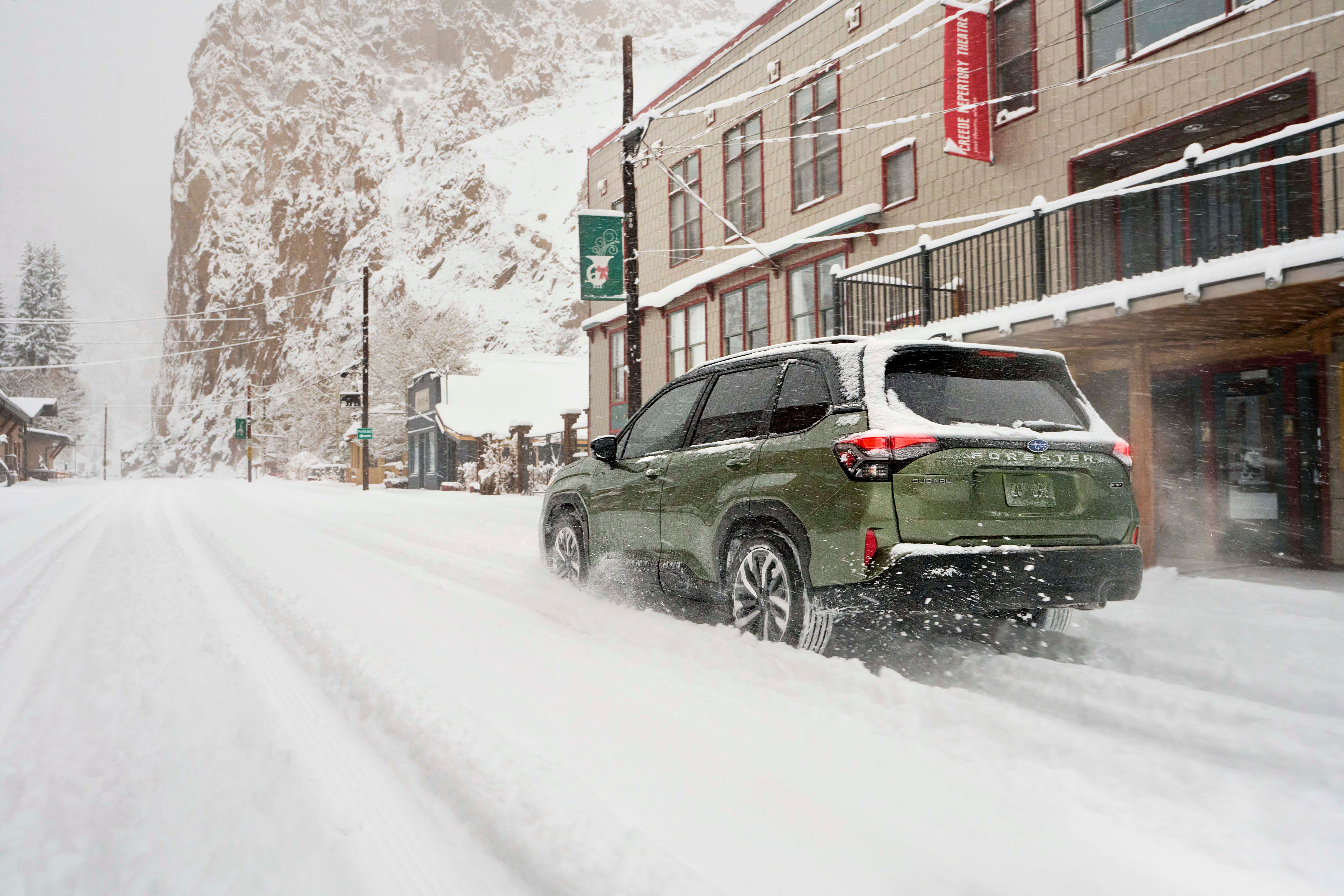 Green 2026 Subaru Forester Hybrid driving through snow in a downtown area.