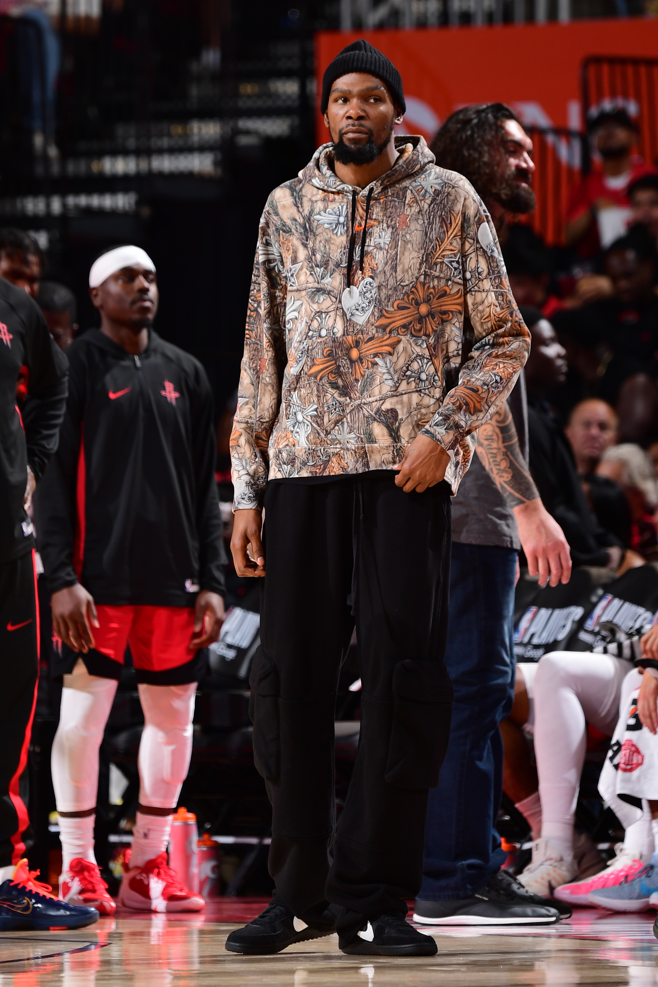 Kevin Durant standing on the basketball court during the NBA Playoffs, wearing a camouflage hoodie and black beanie.