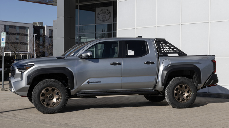 Side view of silver Toyota Tacoma Trailhunter parked in front of a Toyota dealership.